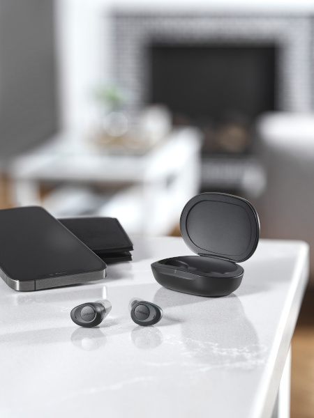 Jabra Enhance Plus hearing enhancing earbuds lying on a table next to the charging case