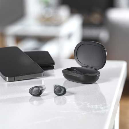 Jabra Enhance Plus hearing enhancing earbuds lying on a table next to the charging case
